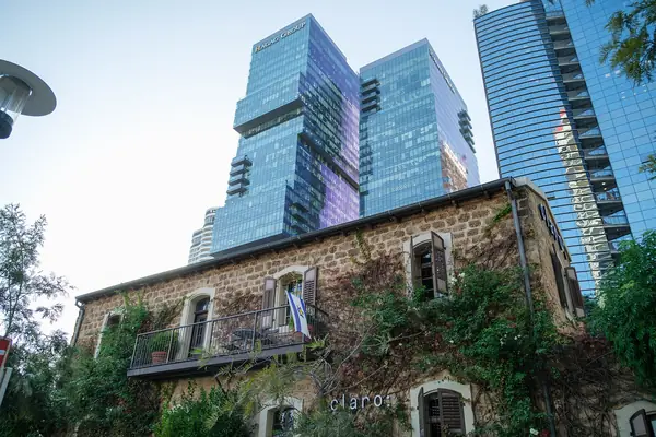 Ivy-clad stone Templar house with glass business towers rising behind it near Sarona, Tel Aviv