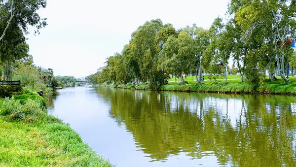 Reflections on the Yarkon river between wooded banks in the park bordering Bavli